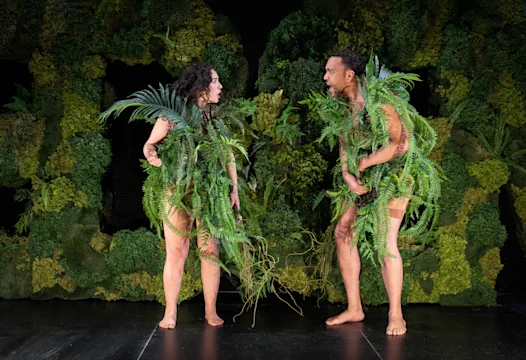 Production photo of On the Evolutionary Function of Shame showing man and woman covered with leaves.