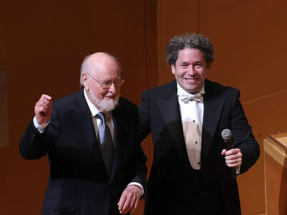 Two men in formal attire stand side by side on a stage; one holds a microphone, and both appear pleased.