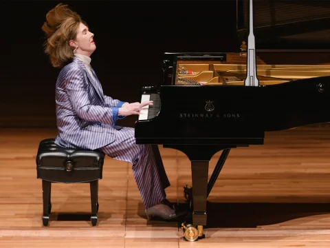 Person in a striped suit passionately playing a Steinway & Sons grand piano on a wooden stage.