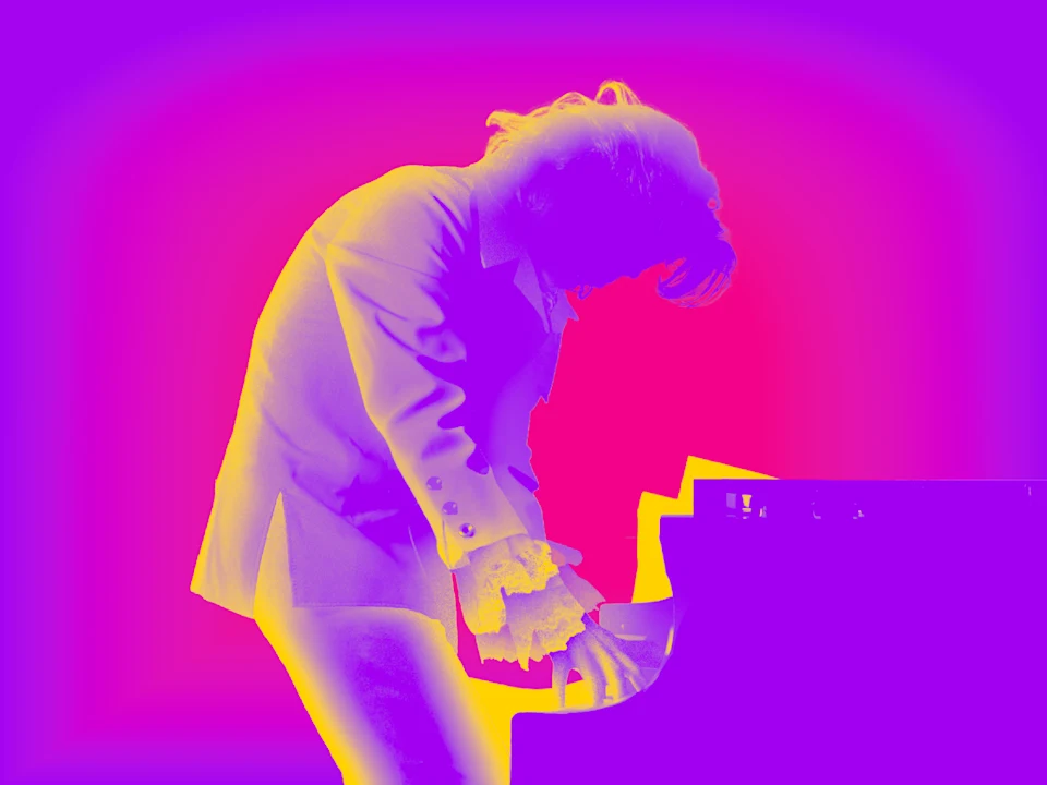 A person in a suit is playing a piano, shown in a colorized purple, pink, and yellow gradient effect.