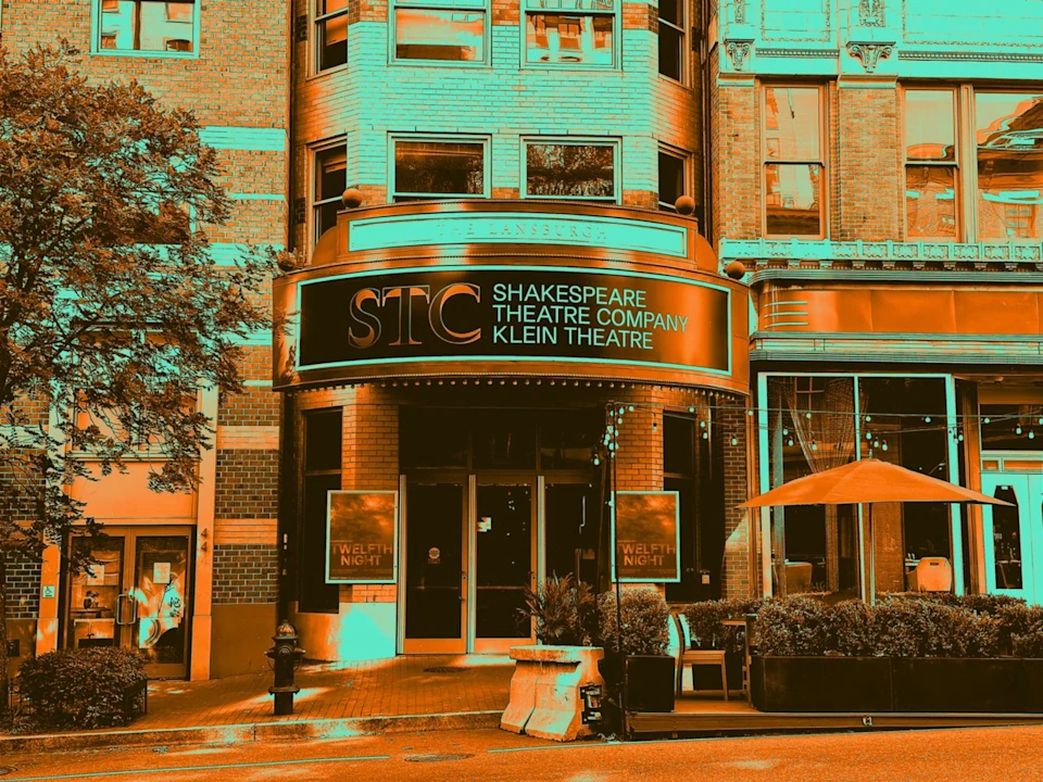 Entrance of the Shakespeare Theatre Company Klein Theatre with a marquee sign above the doors, outdoor seating, and surrounding brick buildings.
