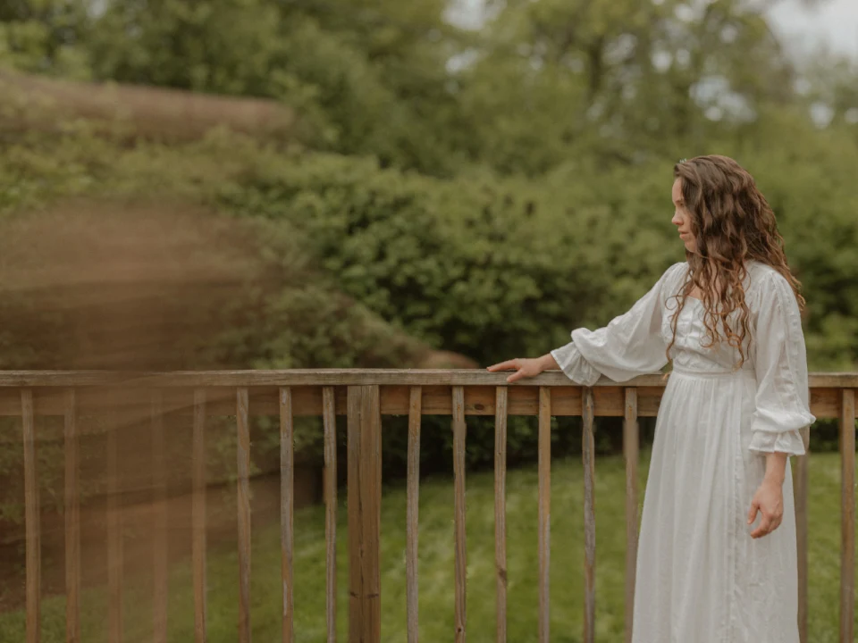 Production shot of Mary’s Wedding in Chicago with Ksa Curry as Mary in a white dress standing on a wooden deck in a lush green garden.