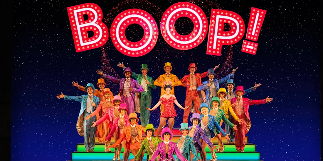 A large group of performers in colorful costumes poses on stage under a bright "BOOP!" sign with illuminated letters.