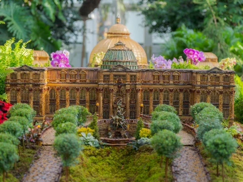 A detailed miniature model of a historical building, surrounded by trees and flowers, with a dome and intricate architectural features.