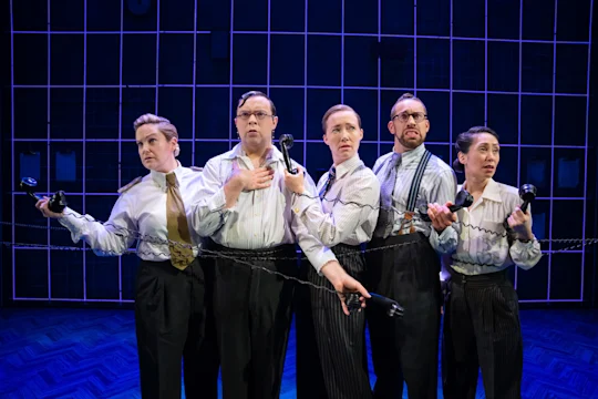 Five people in matching shirts and ties stand in a line, holding old-fashioned telephones, against a blue grid-patterned background.