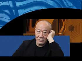 A bald man with a beard wearing a black jacket rests his head on his hand, set against abstract blue and gold geometric backgrounds.