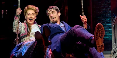 A woman in a floral dress and a man in a blue suit laughing while swinging on rope swings.