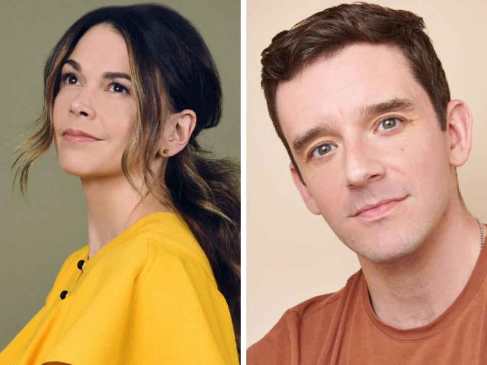 A woman (Sutton Foster) wearing a yellow top and a man (Michael Urie) in a brown shirt are shown in a side-by-side portrait. Both are looking slightly upward.