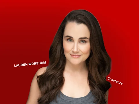 Photo of Lauren Worsham (Constanze) with long brown hair and blue eyes poses against a red background.