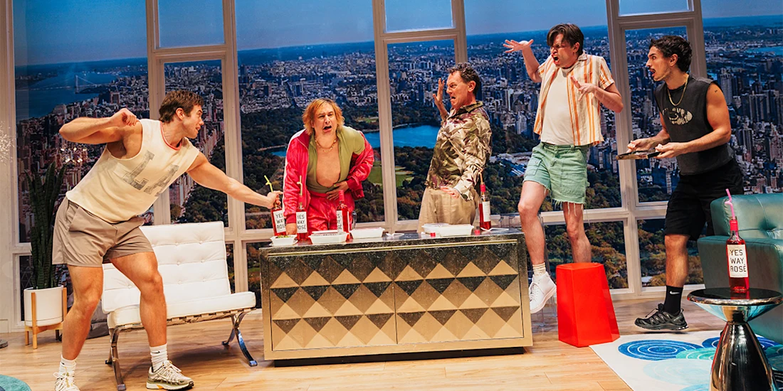 Five men in casual clothes react animatedly in a modern living room with large windows showing a cityscape and park in the background.