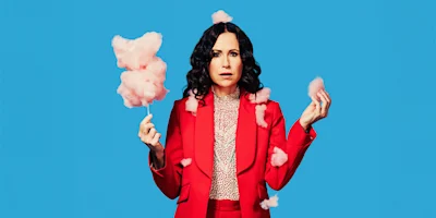 A woman in a red suit holds pink cotton candy against a bright blue background, with cotton candy pieces floating around her.