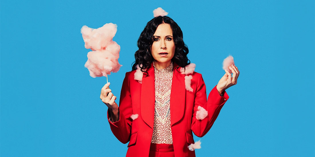 A woman in a red suit holds pink cotton candy against a bright blue background, with cotton candy pieces floating around her.