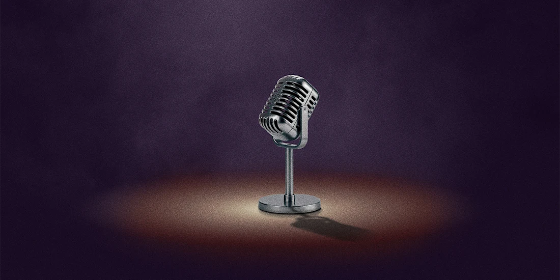 A vintage-style microphone on a stand is spotlighted against a dark, smoky background.