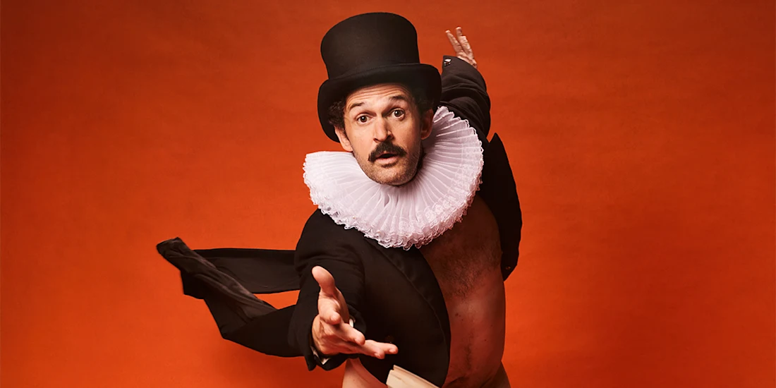 A man in a top hat, ruffled collar, and tuxedo jacket poses dramatically with one arm extended against an orange background.