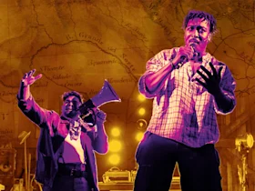 Two performers are on stage. One raises a megaphone while the other speaks into a microphone. They are set against a backdrop of a historical map.