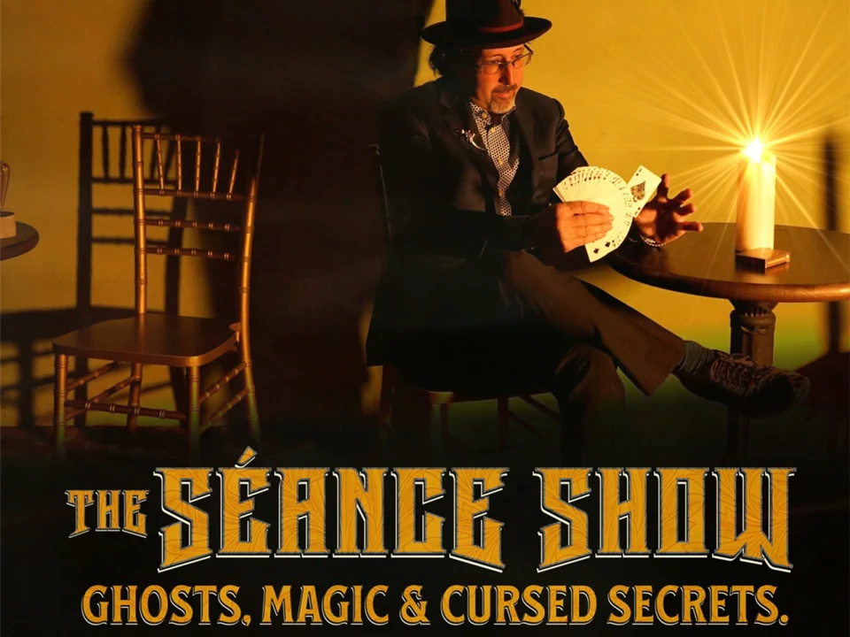 A man in a hat performs a card trick beside a lit candle. The text reads: "The Séance Show: Ghosts, Magic & Cursed Secrets.