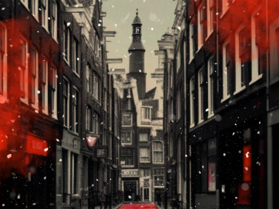 A narrow street between tall, old buildings under snowfall with a prominent clock tower in the background. Red lighting casts a glow on the street and buildings.