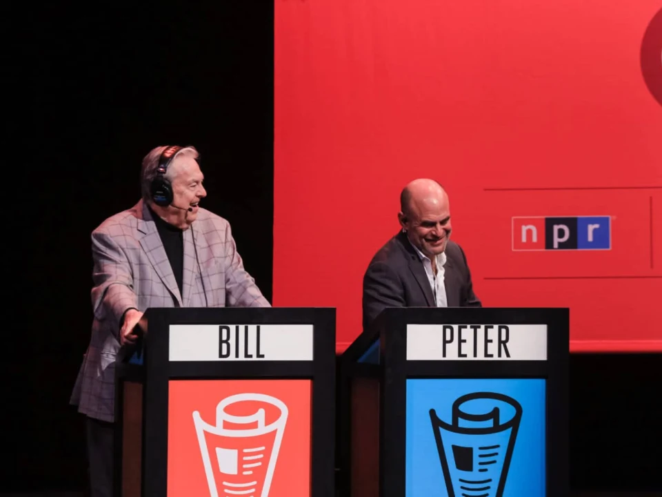 Production photo of Wait Wait...Don't Tell Me! in Chicago  with BILL and PETER behind podiums with microphones and headphones.