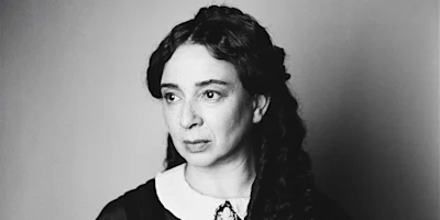 Black-and-white portrait of a woman with long, dark, wavy hair, wearing a white collar and looking slightly to the side with a neutral expression.