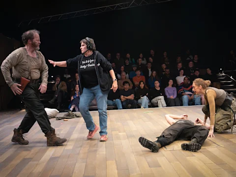 Production photo of The Seat of Our Pants in New York, showing four actors perform an intense scene on stage with a seated audience in the background; one actor is standing, one is pointing, one is kneeling, and one lies on the floor.