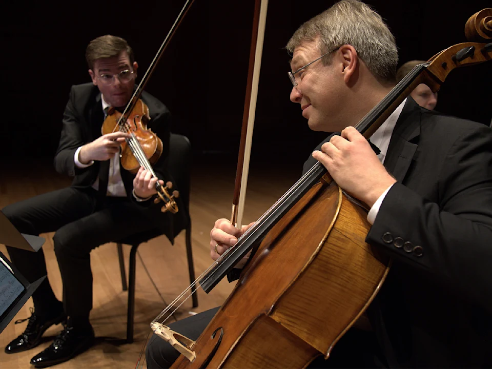 Two musicians in formal attire play a violin and a cello on stage during a performance.