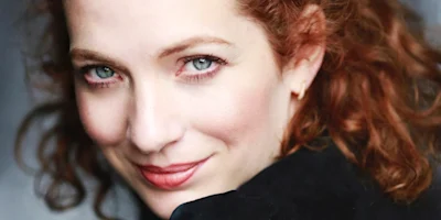 Close-up portrait of a woman with red hair looking directly at the camera.