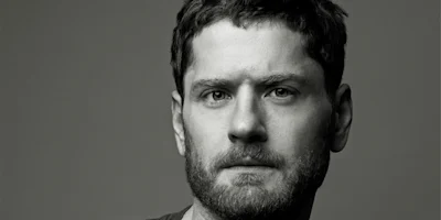 Black and white portrait of a man with short hair and a beard, looking directly at the camera with a neutral expression.
