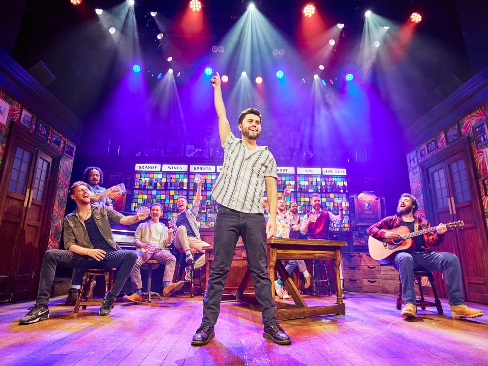 Production shot of The Choir of Man in London, showing cast cheering.