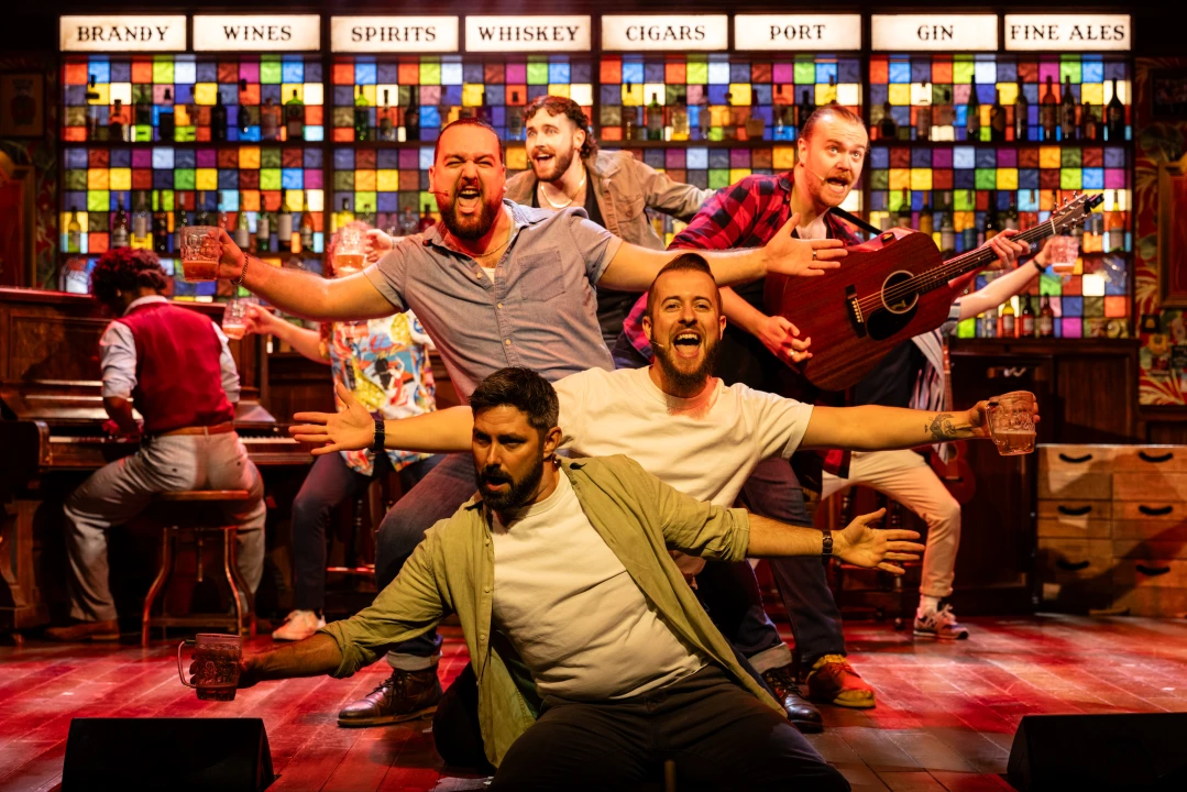 Production shot of The Choir of Man in London, showing cast cheering.