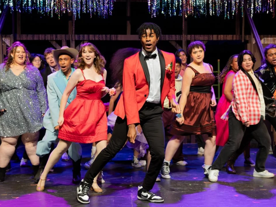 A diverse group of people wearing formal attire perform energetically on stage under hanging streamers.