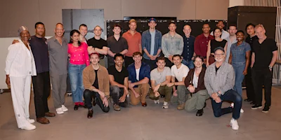 A group of people poses indoors, arranged in two rows, with some standing and others kneeling, all facing the camera.