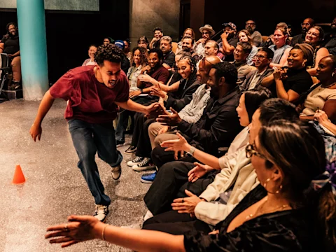 A performer runs past rows of seated audience members, giving high fives and interacting energetically with them during a lively stage event.