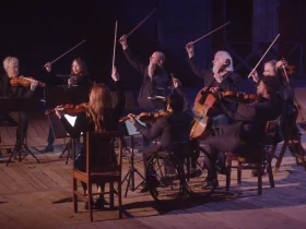 Production shot of Under the Oaks Presents Hills Like White Elephants in Los Angeles, showing group of people playing violin.