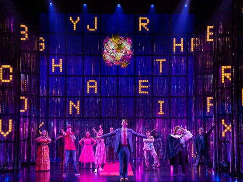 Production photo of How To Dance In Ohio Broadway Reunion Concert in New York City, showing a vibrant musical theater performance featuring a backdrop of illuminated letters and a colorful, suspended globe.