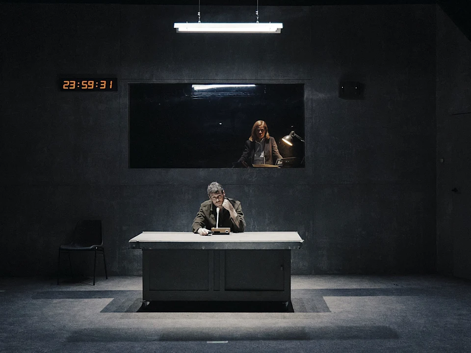 A person lies on the ground while another person stands, holding and pulling their arm in a dimly lit setting.