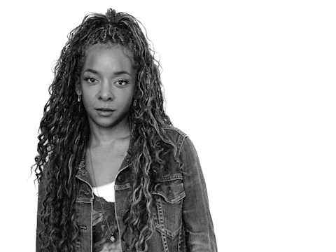 Kara Young wearing a denim jacket stands against a white background, looking directly at the camera.
