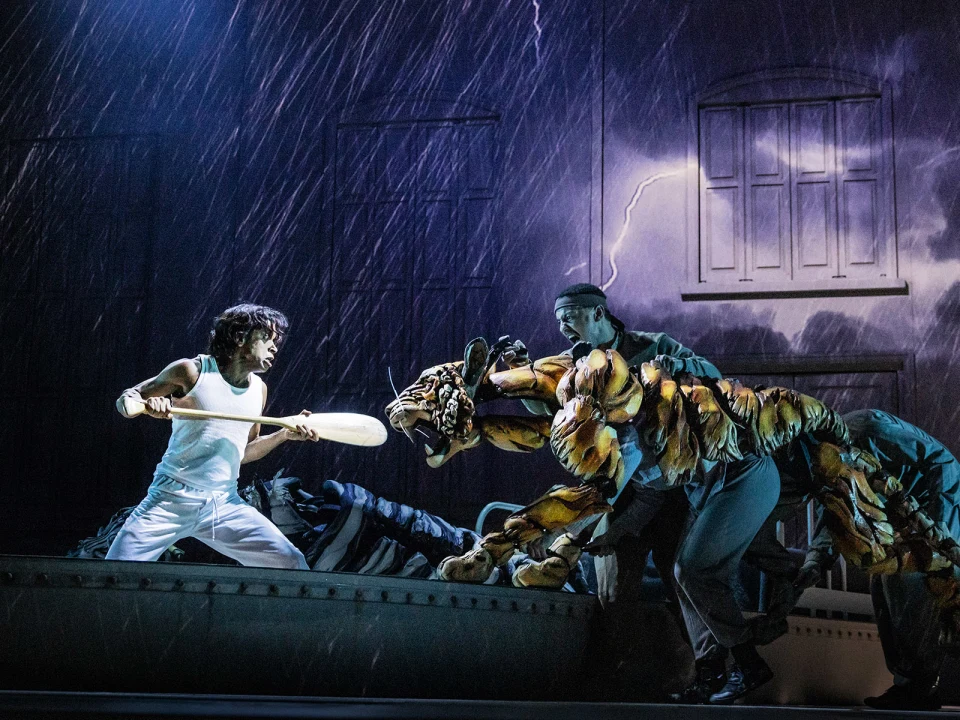 A person in white clothing defends against a tiger puppet operated by two individuals, set against a stormy backdrop with lightning.