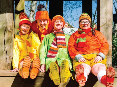 Production shot of Four Go Wild in Wellies in New York, showing ensemble with their colorful winter clothing sitting on a wooden bench.