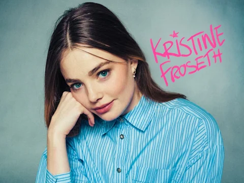 Woman with long brown hair and blue eyes, wearing a blue striped shirt, poses with head resting on hand against a blue background. "Kristine Froseth" written in pink lettering.