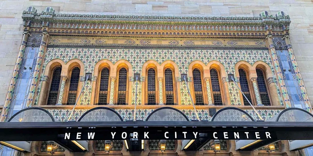 Ornate facade of New York City Center featuring tall arched windows, colorful tile work, and a marquee displaying the venue’s name.