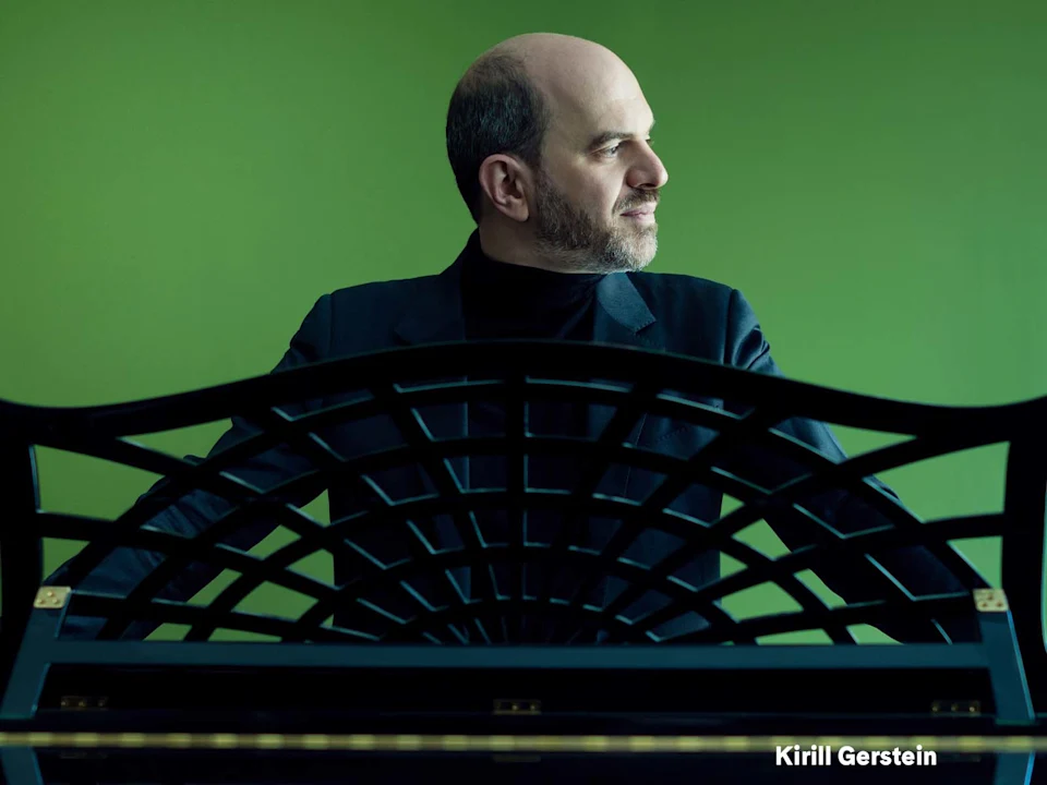 A man in a dark suit sits behind a black piano with a decorative music rack, against a green background. Text in the lower right corner reads "Kirill Gerstein.