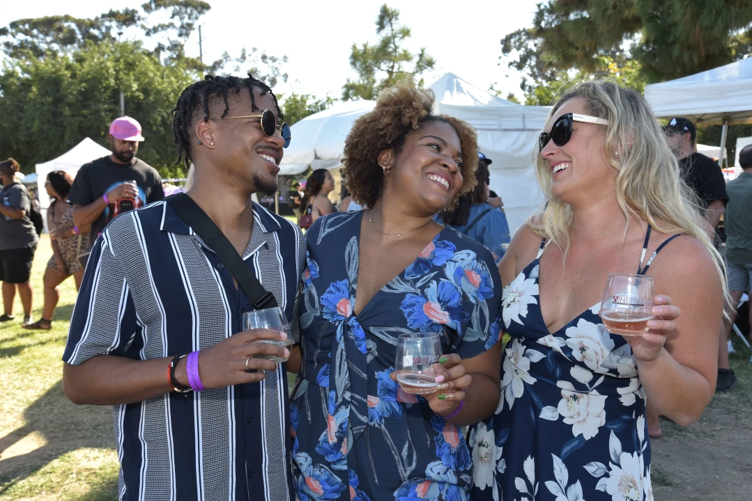 Three women enjoying drinks and conversation at the 19th Annual LAWineFest, smiling and laughing together.