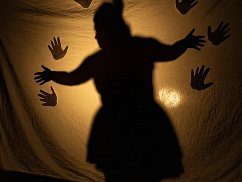 Silhouette of a person with outstretched arms cast on a backlit sheet, surrounded by handprint shadows.