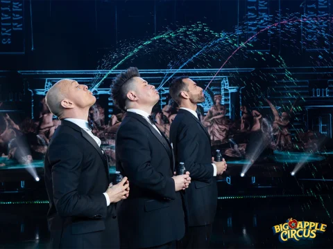 Three performers in suits simultaneously spout water streams from their mouths in a choreographed act.