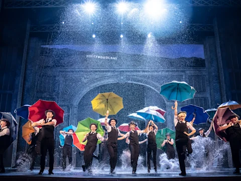 The full company dance with colourful umbrellas in the rain in Singin' in the Rain