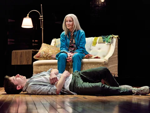 Production photo of We Had a World in New York, showing a boy laying on the floor and a woman seating on a couch.