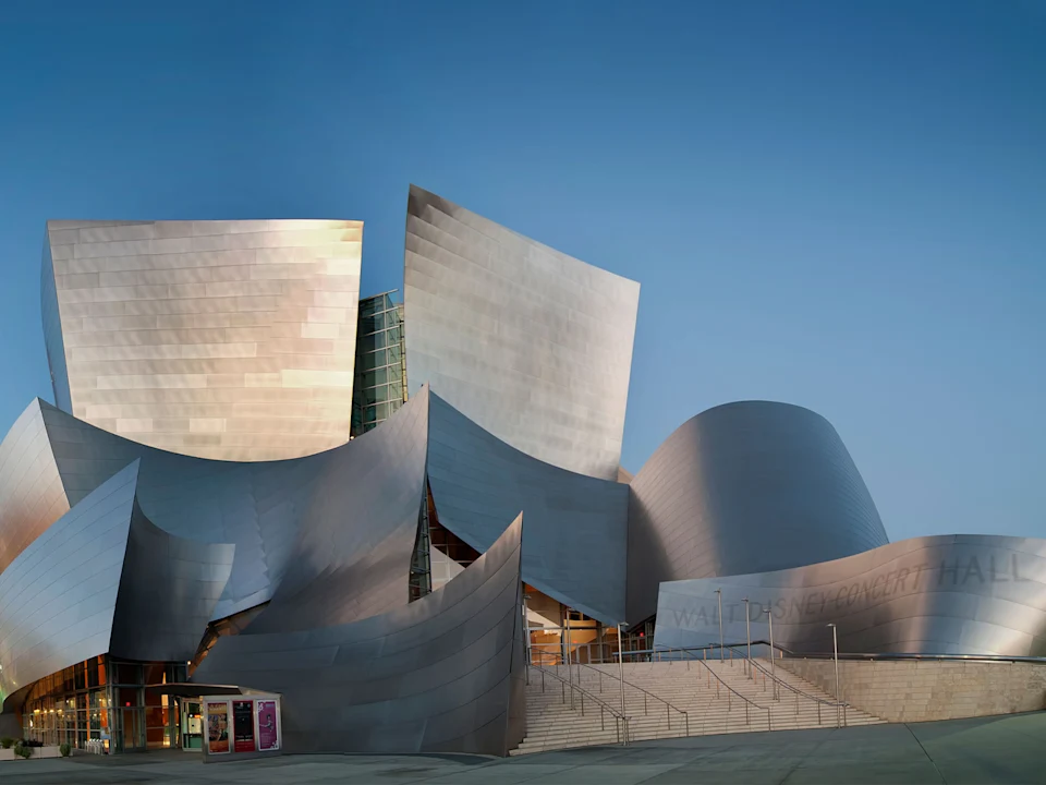 The Walt Disney Concert Hall with its distinctive metallic exterior and curved architectural design is shown against a clear sky.