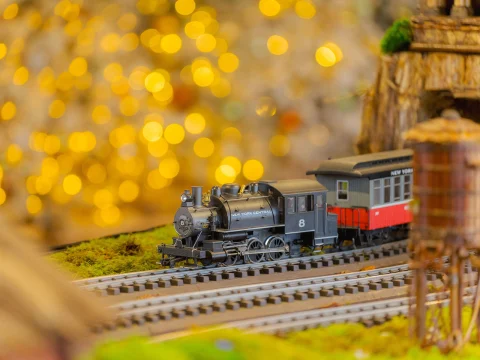 Model steam train on a track with a colorful bokeh background and small buildings nearby.