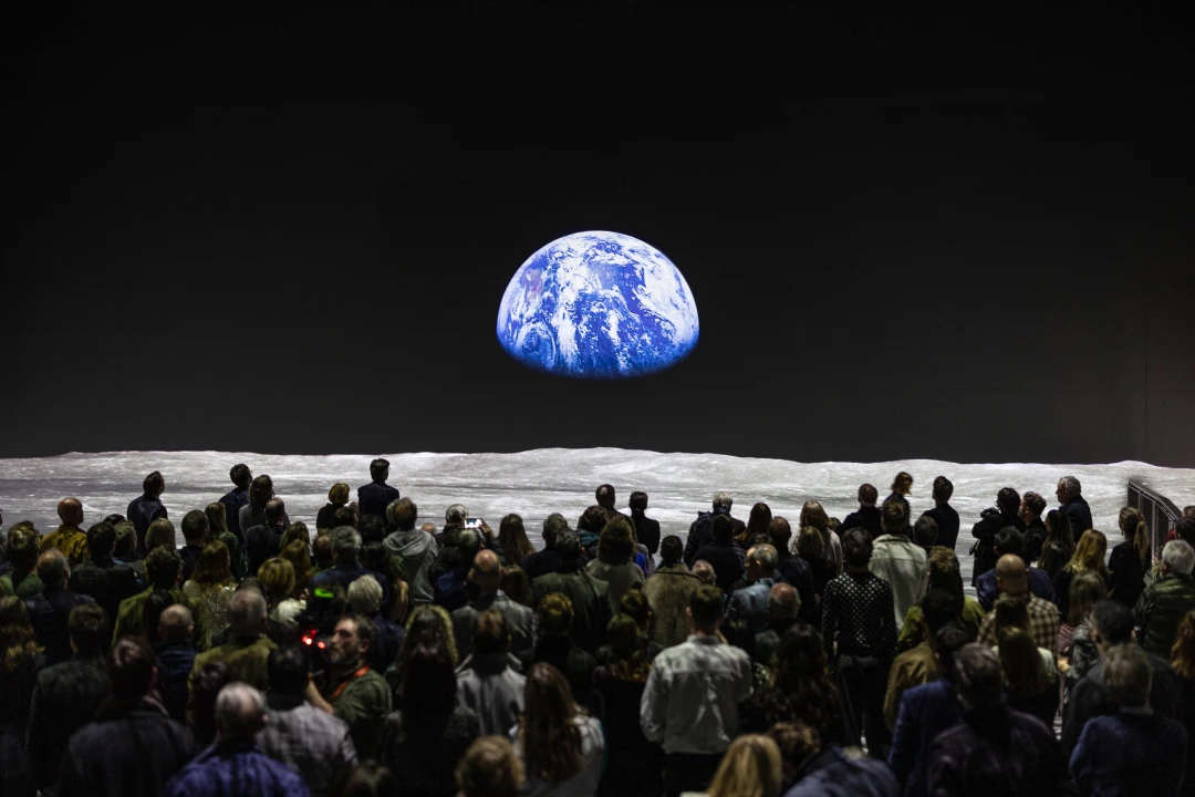 Picture of The Moonwalkers in London, showing an audience watching a projection of the earth from the moon's surface