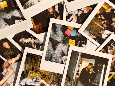 A pile of Polaroid photos showing people celebrating, toasting drinks, decorations, and festive scenes, suggesting a New Year's Eve party.